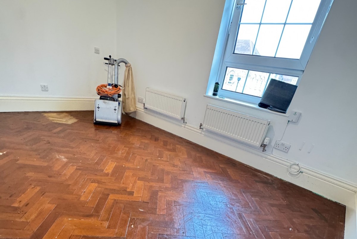 Parquet Floor Sanding in Egham on a dark oak herringbone parquet bedroom floor, with a sanding machine ready to strip the old finish.