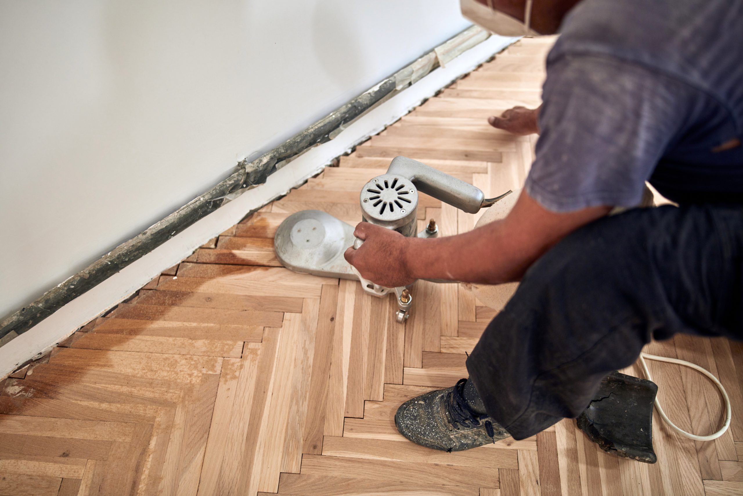 Parquet Floor Sanding in Egham with a technician edge-sanding a light oak herringbone parquet floor along the skirting board.