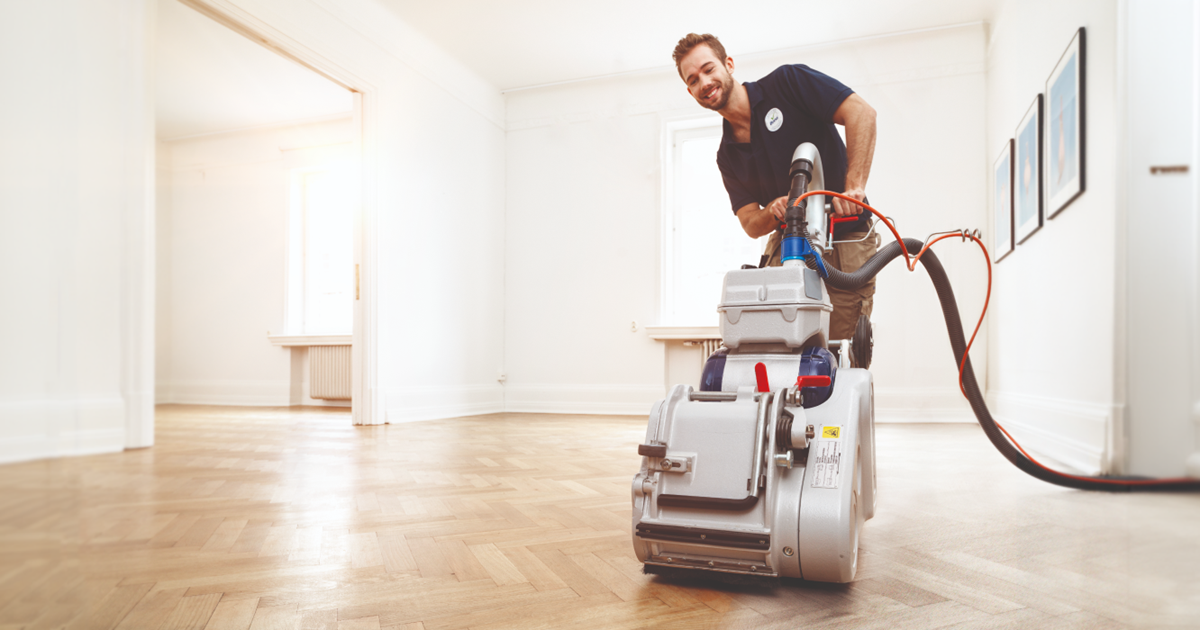 Professional Parquet Floor Sanding in Egham on a light oak herringbone parquet floor, using a dust-controlled belt sander in an empty room.
