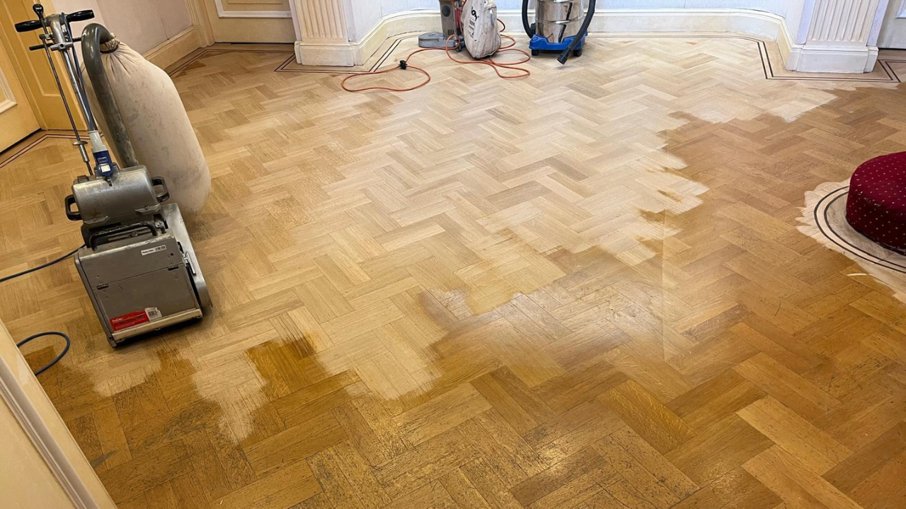 Parquet Floor Sanding in Egham on an oak herringbone parquet floor, showing the mid-sanding stage where old, yellowed finish is being removed for restoration.