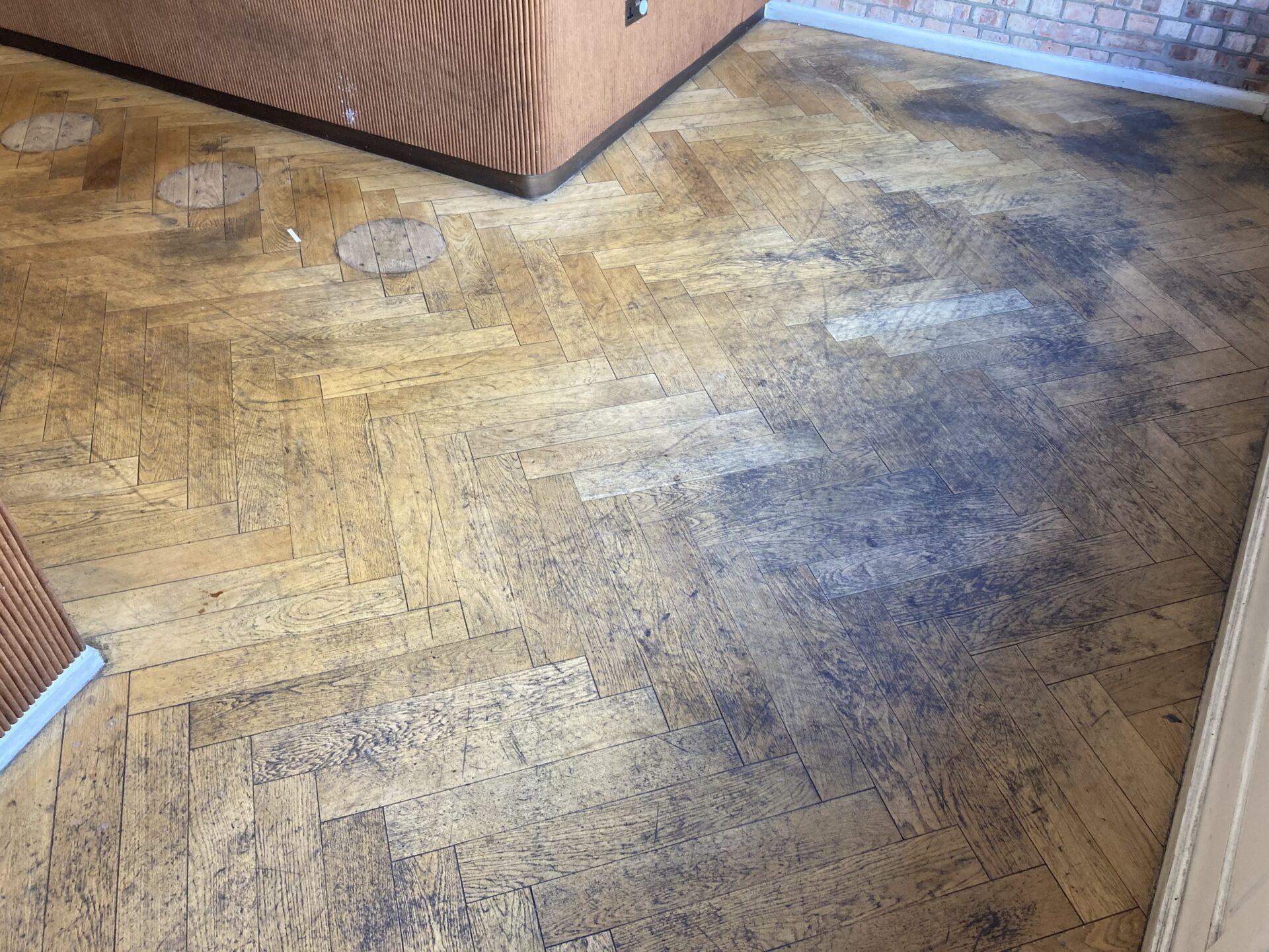 Parquet Floor Sanding in Egham on a heavily worn oak herringbone parquet floor with dark traffic stains and circular marks before restoration.