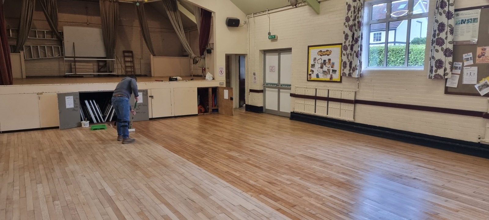 Commercial Floor Sanding in Egham on a maple strip hardwood community hall floor, with a technician applying finish after sanding.