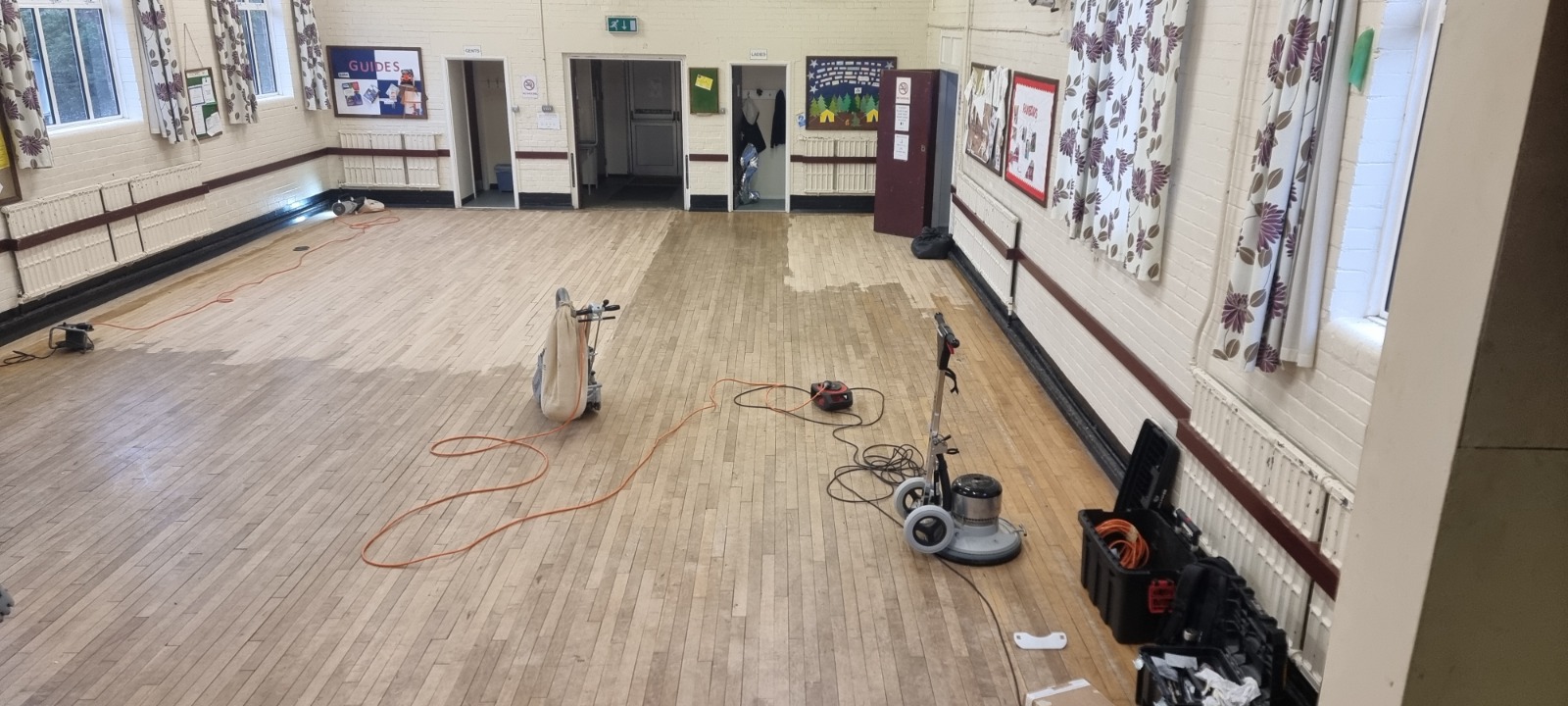 Commercial Floor Sanding in Egham on a maple strip hardwood hall floor in progress, with sanding machines and cables laid out during restoration.