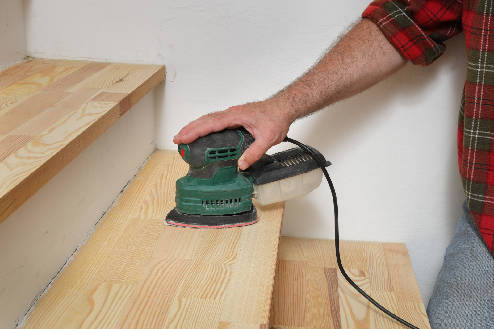 Commercial Floor Sanding in Egham on pine softwood stair treads, with a technician using a detail sander to smooth the steps.